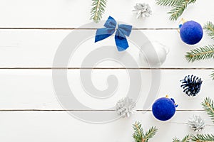 Christmas card with blue balls, fir tree branches, gift boxes, ornaments on wooden white background. New year holiday festive