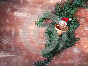 Christmas card with branches of a Christmas tree and a little santa among the branches on a rustic background