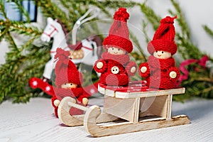 Christmas card. Bright red toys kids in knitted clothes on Santa`s sleigh on the background of a Christmas tree and a toy horse.