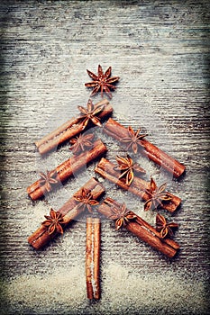 Christmas card with Christmas fir tree made from spices cinnamon sticks, anise star and cane sugar on rustic wooden background