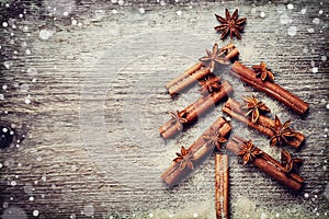 Christmas card with Christmas fir tree made from spices cinnamon sticks, anise star and cane sugar on rustic wooden background