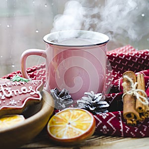 A cup of hot tea stands on a wooden table next to a wooden plate on which are gingerbread cookies made from orange slices against