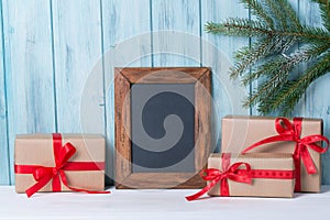 Christmas card with empty chalkboard and gift boxes, wooden background with fir tree branch