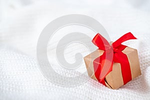 Christmas card with gift box red ribbon on white knitted sweater background. Copyspace