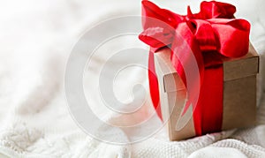 Christmas card with gift box red ribbon on white knitted sweater background. Copyspace