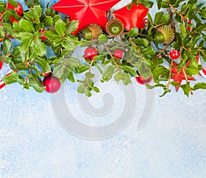 Christmas card with green holly leaves, red berries and Xmas decorations on blue background with copy sace