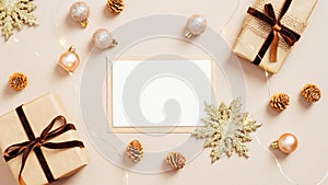 Christmas card mockup on pastel beige background with gift boxes, golden balls and xmas decorations. Flat lay, top view. Minimal