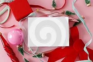 Christmas card mockup, pink flat lay. Empty card with space for text and red bow, little trees, baubles, ribbons on pink