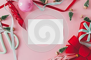 Christmas card mockup, pink flat lay. Empty card with space for text and red bow, little trees, baubles, ribbons on pink