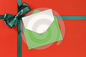 Christmas card, red gift wrap paper background, green gift ribbon bow, envelope, copy space