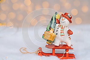 Christmas card with red wooden Santa Claus sleigh with snow man, and Xmas tree balls over blurred light background