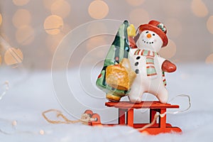 Christmas card with red wooden Santa Claus sleigh with snow man, and Xmas tree balls over blurred light background
