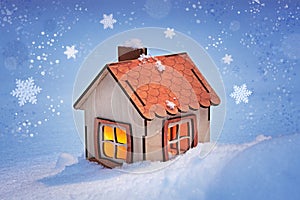 Christmas card, a small model of a wooden house with a cozy light in the windows on a winter snowy evening