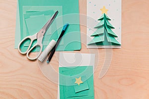 Christmas card, a stack of colored paper, scissors and glue. Child making Christmas card from paper. Step 1