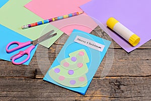 Christmas card tutorial. Paper greeting card with text Merry Christmas, pencil, glue stick, colored paper sheets, scissors