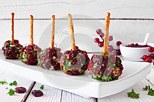 Christmas cheese ball appetizers with cranberries, pecans and herbs, close up on a serving plate against white wood