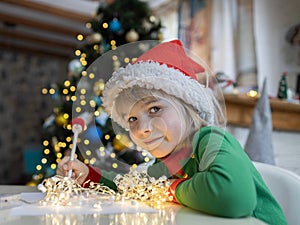 Christmas child writes a letter to Santa while sitting at the table against a bokeh background
