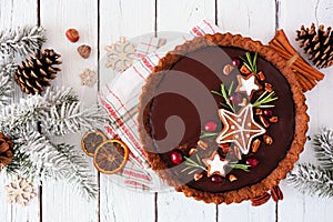 Christmas chocolate gingerbread tart. Overhead view table scene with a white wood background.