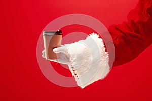 Christmas coffee. The Santa hand holding cup of cofee isolated on a red background with space for text