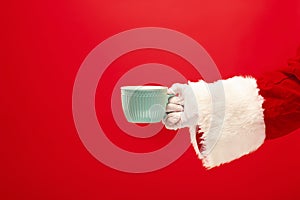 Christmas coffee. The Santa hand holding cup of cofee isolated on a red background with space for text