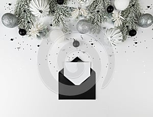 Christmas composition, black envelope, white and silver decorations, fir tree branches, silver stars confetti on white background.