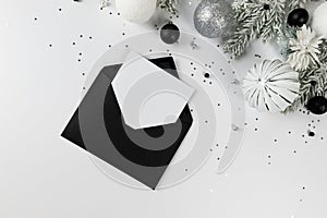 Christmas composition, black envelope, white and silver decorations, fir tree branches, silver stars confetti on white background.