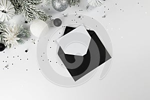 Christmas composition, black envelope, white and silver decorations, fir tree branches, silver stars confetti on white background.