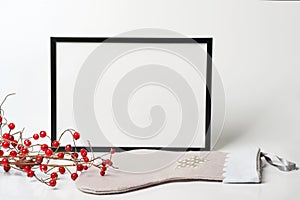 Christmas composition. Black frame and christmas sock with branches with red berries on white background.