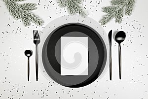 Christmas composition, black plate and cutlery, white card, fir tree branch, silver stars confetti on white background.