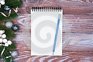 Christmas composition with blank notepad, pencil for wish list and Christmas decoration on wooden background. Flatlay. Top view.
