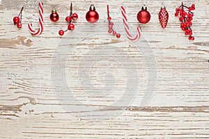 Christmas composition border on white wooden background. Red holly berries, baubles and candy. Minimal Xmas flat lay top view