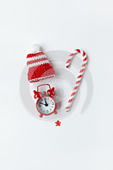 Christmas composition, cane candy, small analog clock, striped hat, star, laid out in shape of heart on white background. Minimal