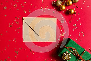 Christmas composition. Envelope, wrapped gift, toys on red background with golden confetti. new year concept. Greeting card, xmas