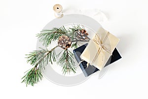 Christmas composition. Festive wrapped Christmas gift boxes with pine branch with cones and silk ribbon on white table