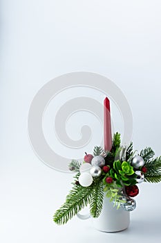 Christmas composition of fir and balls with a red candle in a white cup on a white background with space for writing text