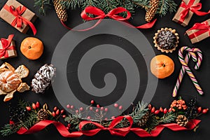 Christmas composition of fir branches, pine cones, berries, gifts and red slack, on black stone background