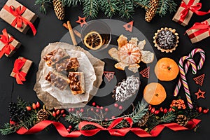 Christmas composition of fir branches, pine cones, berries, gifts and red slack, on black stone background