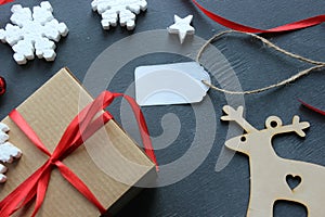 Christmas composition. Gift box with red satin ribbon, wood and snowflakes on black background. Tag, white label for text