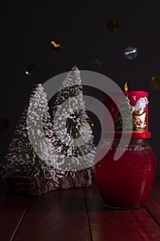 Christmas composition with glass globe containing snow and red glitter, Christmas candle and snow-covered fir trees