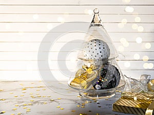 Christmas composition - glass Xmas tree with gold, white and black balls,  bauble and toys, new Year gifts with lights on light