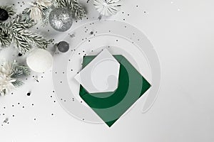 Christmas composition, green envelope, white and silver decorations, fir tree branches, silver stars confetti on white background.
