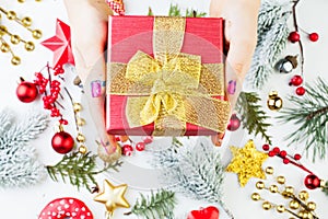 Christmas composition with hand holding gift red gift box with golden ribbon and bow above Xmas decorations background.