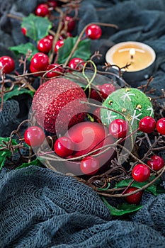 Christmas composition with holly, holiday balls and candle on dark background, vertical, copy space