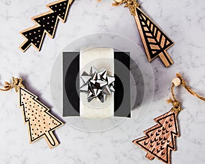 Christmas composition made of black gift box with silver ribbon and wooden christmas tree on marble background, flat lay, top view