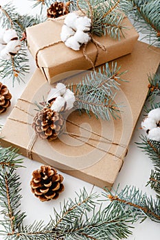 Christmas composition made of presents decorated with fir tree branches, cotton, bumps on white wooden background, table.