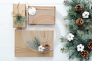 Christmas composition made of presents gifts decorated with fir tree branches, cotton, bumps on white wooden background, table.