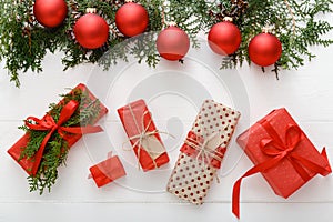 Christmas composition made of red Christmas gifts, red bauble decorations, fir tree branches on white wooden table background.