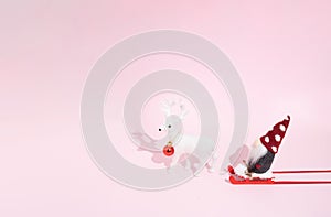 Christmas composition on a pastel pink background. Santa on a red sled and one white reindeer, red decoracion bauble. Xmas and photo