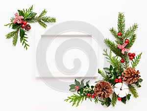 Christmas composition  with photo frame, cotton flower, branches of spruce and holly with red berries on white background. Merry