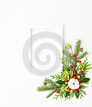 Christmas composition  with photo frame, cotton flower, branches of spruce and holly with red berries on white background. Merry